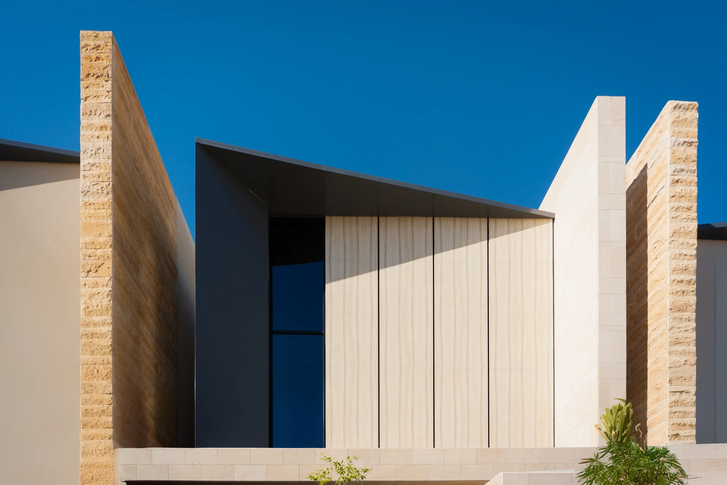 A contemporary villa in Arjan, Dubai, its stone facade and timber screens against a clear blue sky