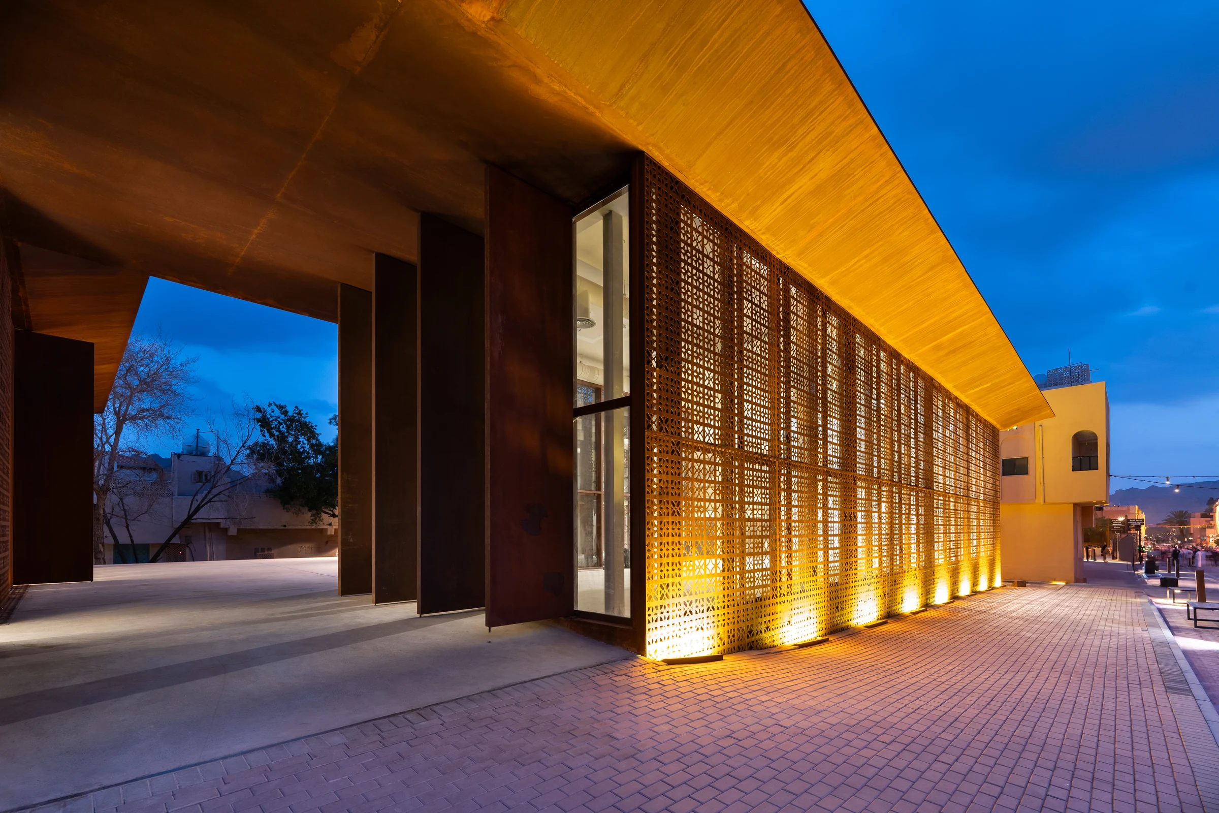 DesignSpace AlUla at blue hour, the colonnade and perforated corten screen lit warm against a deep blue sky