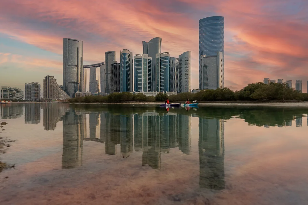 The Abu Dhabi skyline reflected in still water under a pink sunset, photographed for Q Holding