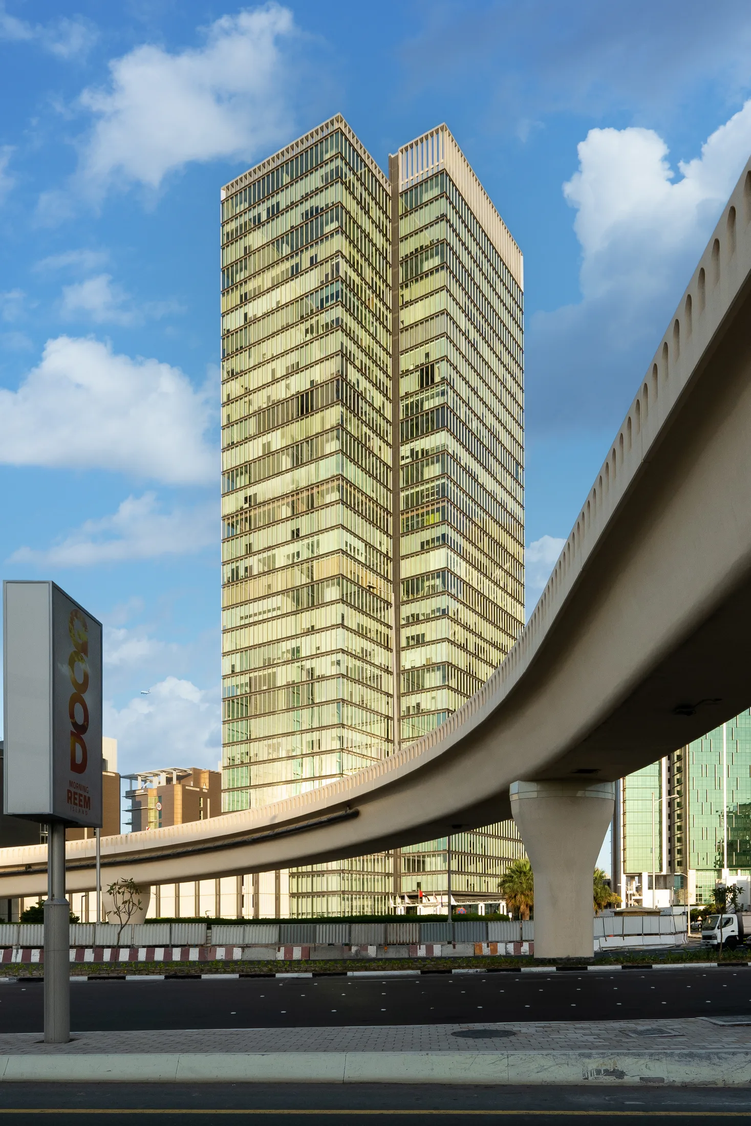 A glass tower in Abu Dhabi seen behind the curve of an elevated road, photographed for Q Holding