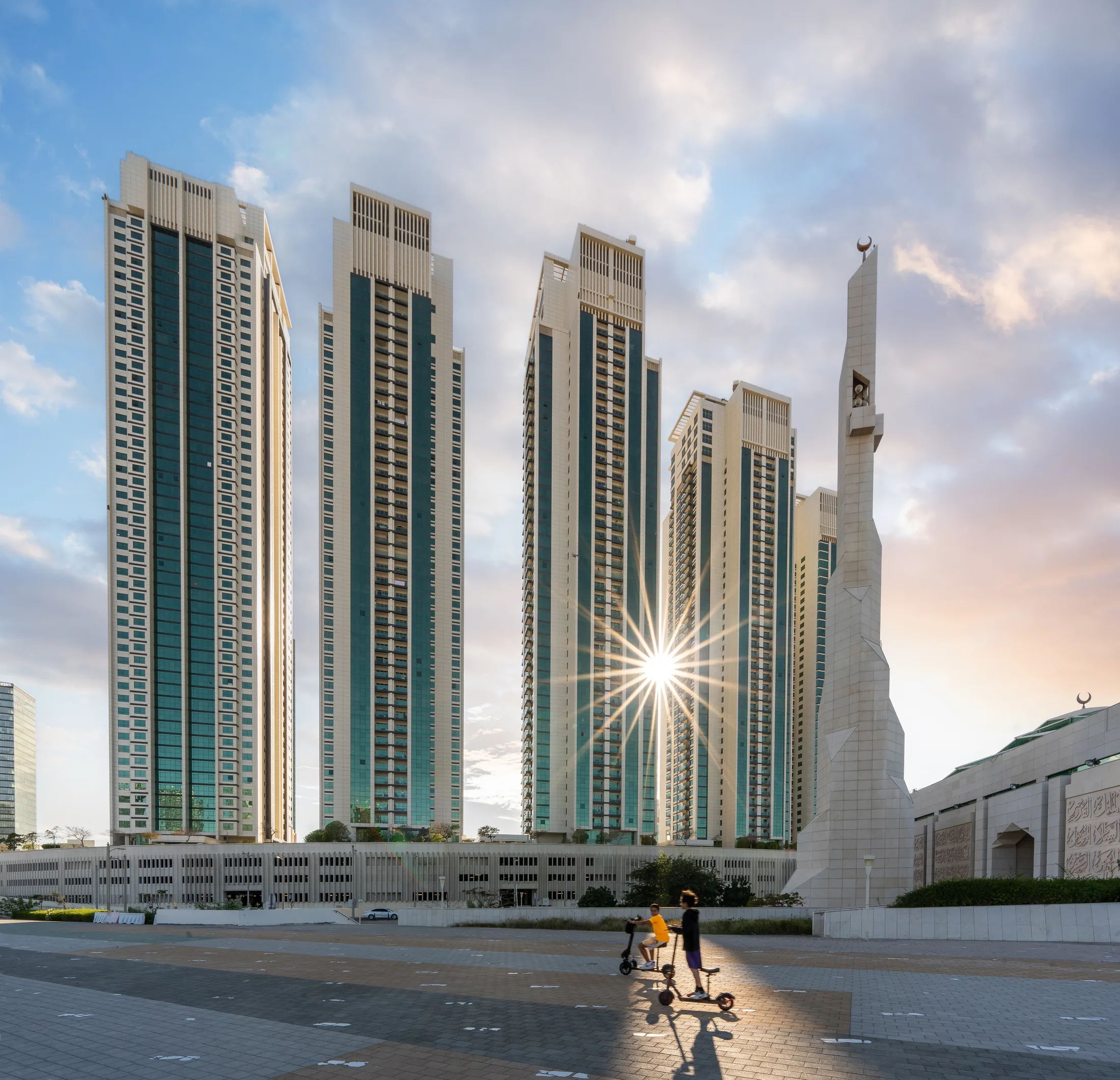 Residential towers in Abu Dhabi with the sun breaking between them and the monument beyond, photographed for Q Holding