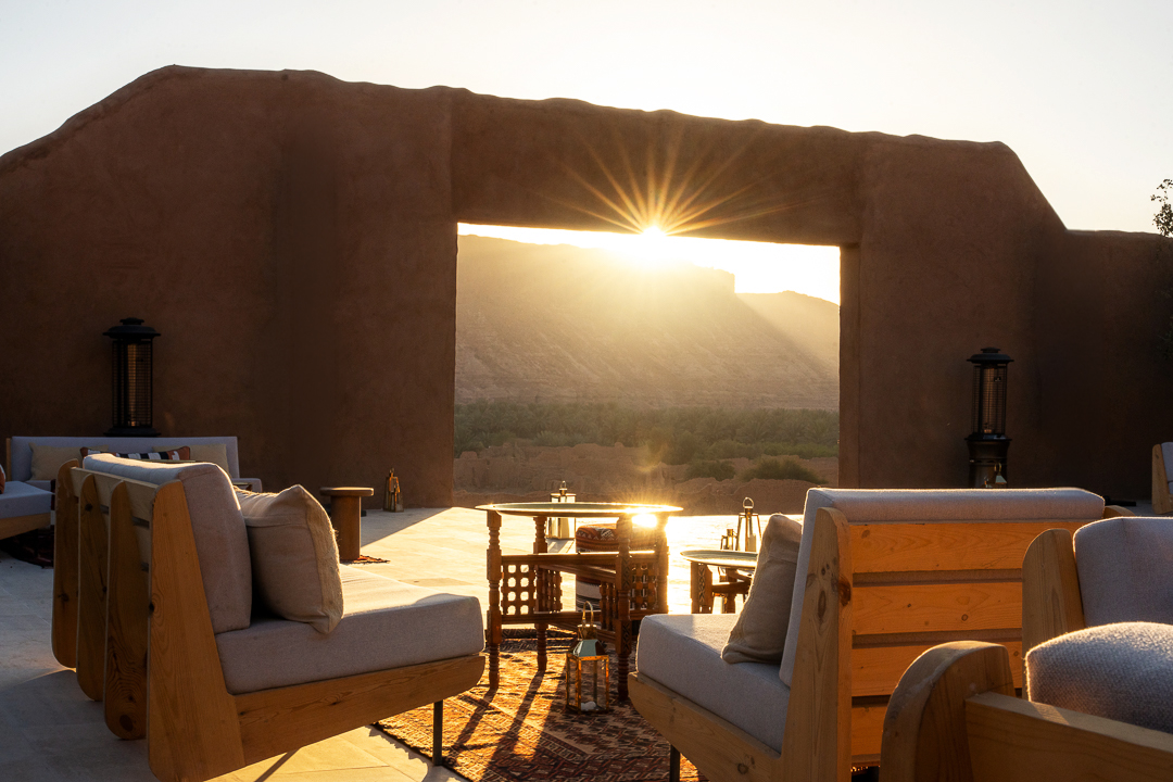 The lounge terrace at Dar Tantora, AlUla, framed by a mud brick archway at sunset