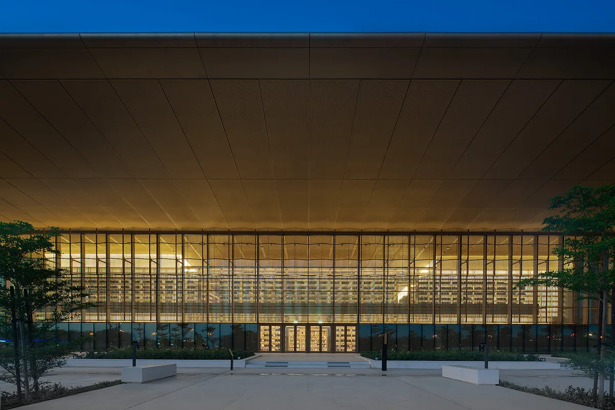 The lit screen elevation of House of Wisdom, Sharjah, at night, warm interior light against the evening sky